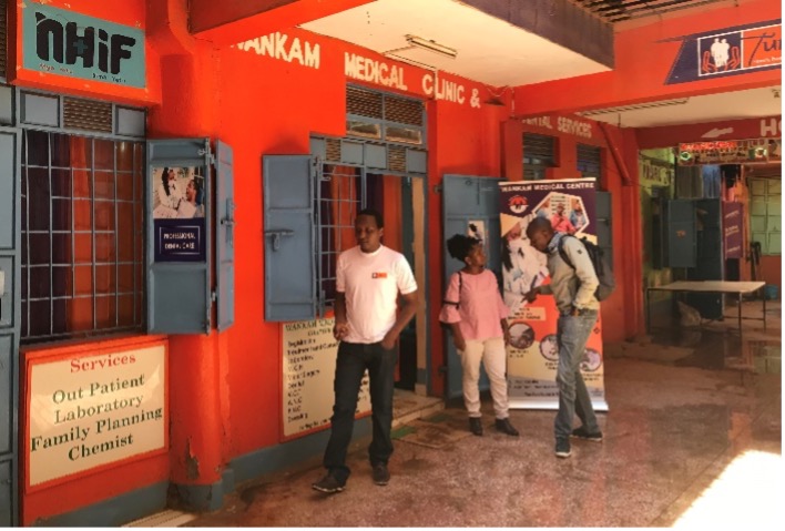 Three people stand in front of a clinic that says 'Wankam Medical Clinic and Dental Services'.