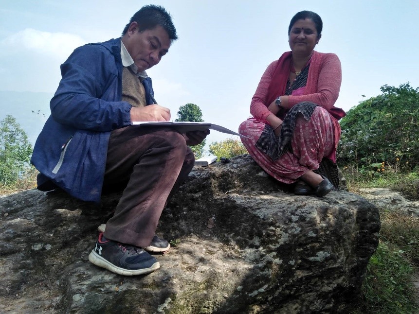 In the picture is a man and a woman sitting down on a large rock