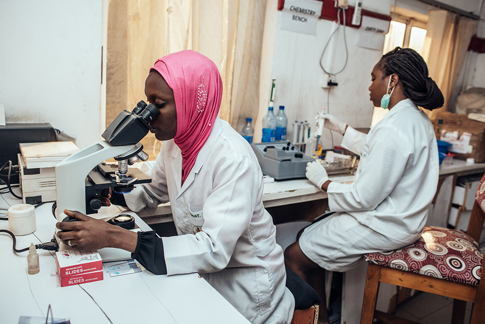 Woman looking through a microscope and another woman using a pipette in a lab in Kano. 