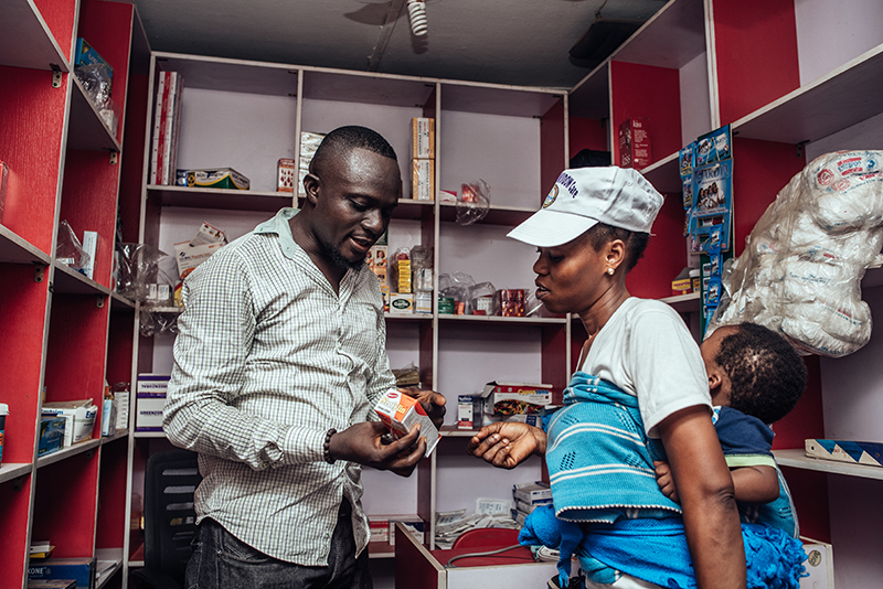 Drug shop owner in Lagos talking to a female client about a product.
