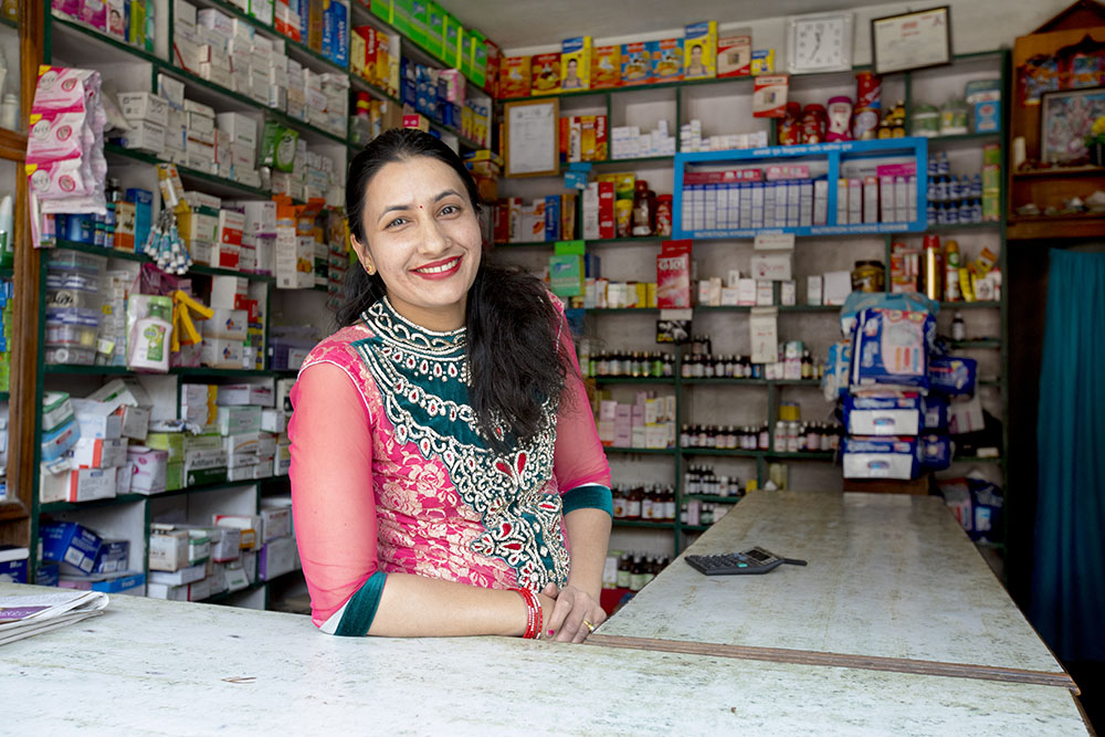Female drug shop owner standing at the counter and smiling at the camera.