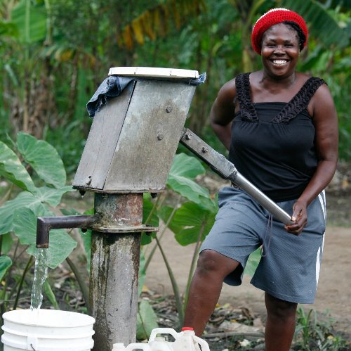 A woman from Haiti pumps water into a bucket