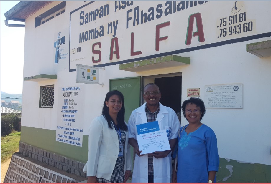 Representatives from SALFA and AccèsBanque Madagascar stand in front of the building holding the certificate of excellence. 