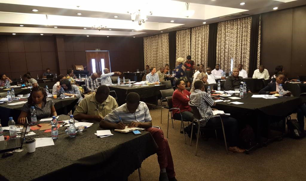 Participants sitting at tables in a conference room at the TMA workshop in Tanzania.