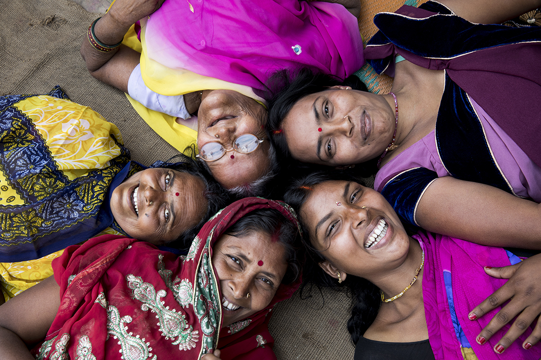 Five Indian women lying down in a circle smiling up at the camera