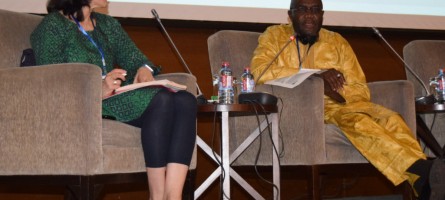 Jeanna Holtz and Dr. Karamoko Nimaga sit in chairs on a stage as they present.