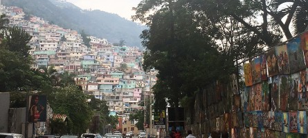 Picture of of a street in Port au Prince, Haiti with cars on the road and rows of houses on a hill in the background. 