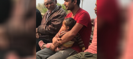 A man holding his young child while listening to a discussion