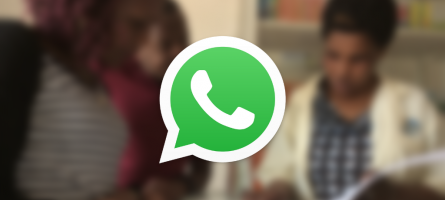 WhatsApp logo over a blurred image of a female health worker talking to a man and a woman