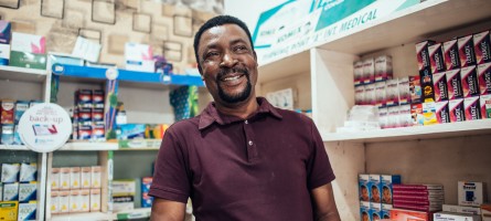 A man smiling and standing behind the counter of a drug shop