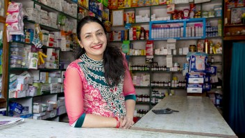 Female drug shop owner standing at the counter and smiling at the camera.