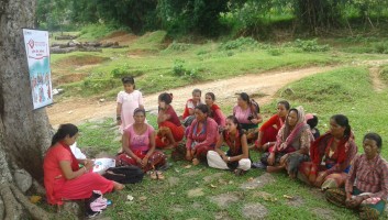 Community change agent conducting a session in a village sitting on the floor in a circle with other women