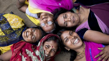 Five Indian women lying down in a circle smiling up at the camera
