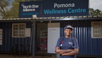 A woman with a stethoscope stands in front of a blue box clinic that says "North Star Alliance welcomes you" and "Pomona Wellness Centre"
