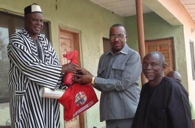 John Enger and Dr. Gbillah hand a bag of campaign materials to HRH Dominic O. Akpe.